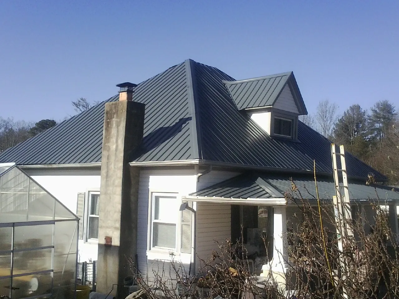 Dark blue standing seam metal roof on a white farmhouse with dormer — Slate & Tile Roof Repair by Roofing Brothers in Cranston