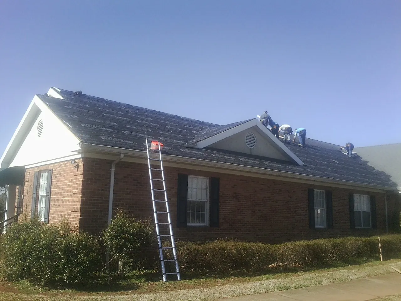 Crew tearing shingles off a brick ranch roof with a ladder set — Emergency Roof Repair work by our crew in Cranston