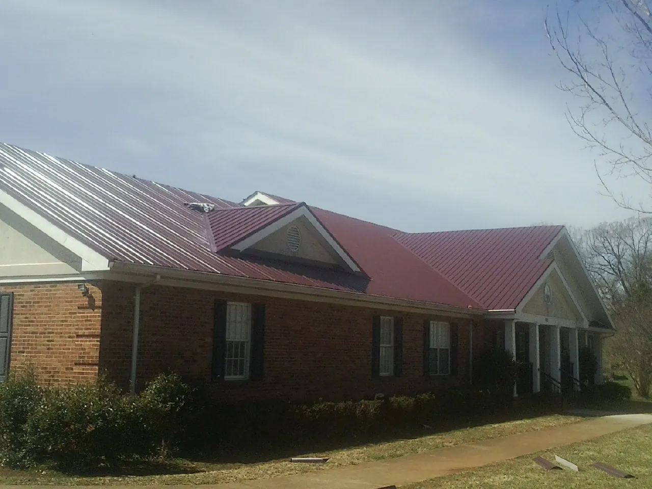 Red metal roof with gabled entries on a long brick building, from a Hail Damage Roof Repair job in Cranston