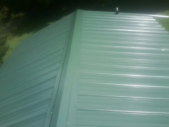 New green metal panels meeting at the ridge of a roof — Flat Roof Repair work by our crew in Cranston