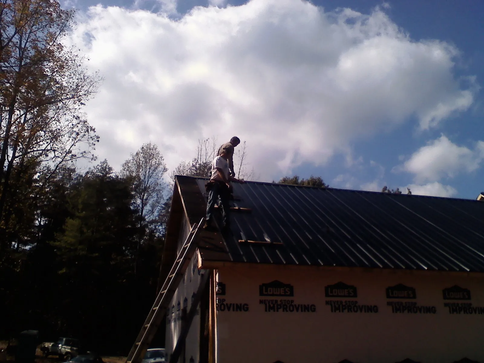 Roofer fastening dark metal panels high against a cloudy sky, from a Roof Inspection job in Cranston