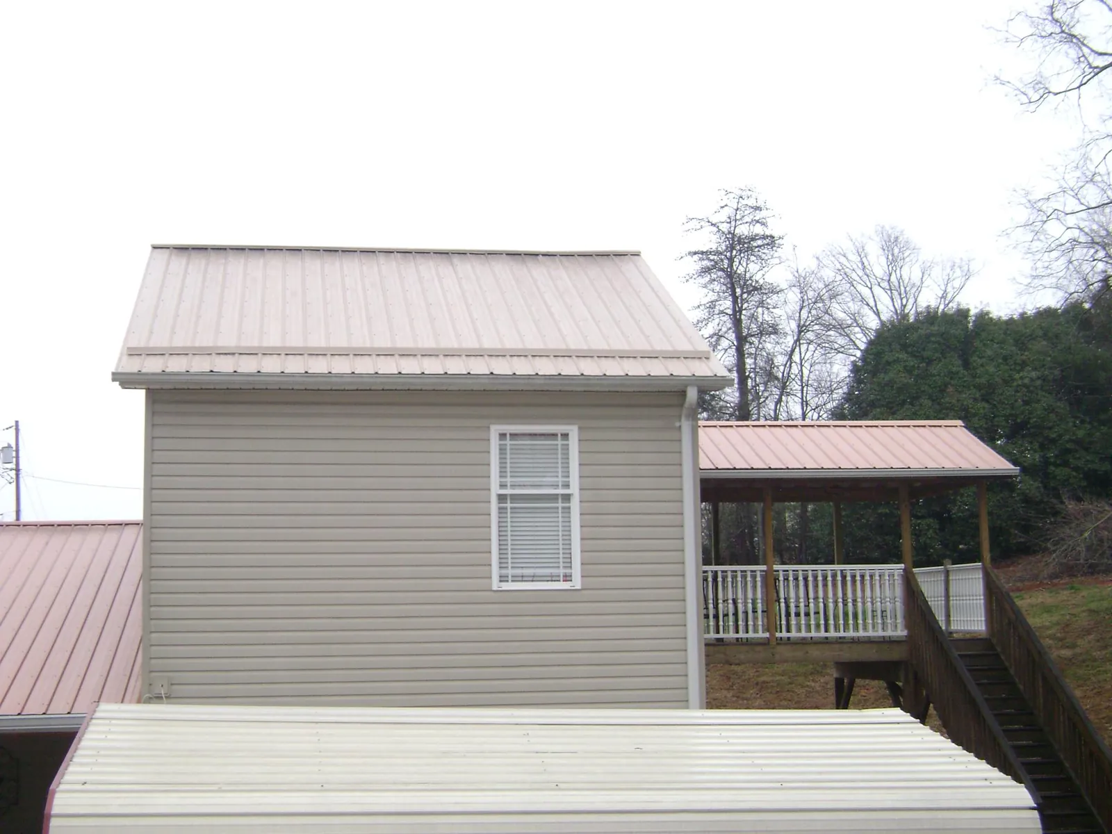 Tan metal roofs on a two story addition and attached porch, from a Roof Replacement job in Cranston