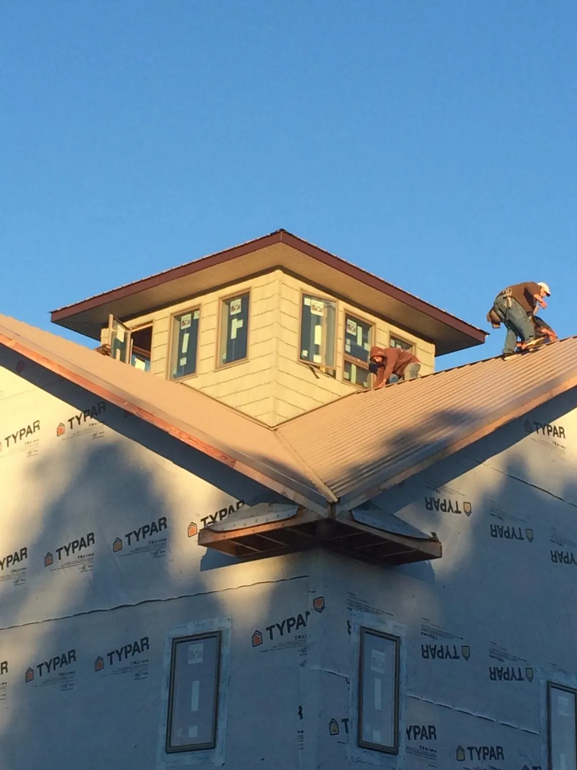 Roofers working around a rooftop cupola on a new metal roof at sunset — Roof Waterproofing in Cranston by Roofing Brothers